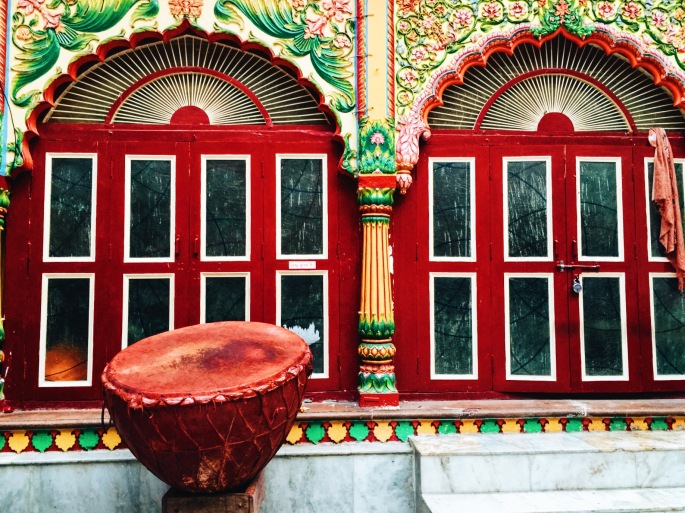 A huge drum, used in religious festivals, placed in front of a colored temple door in Mathura.